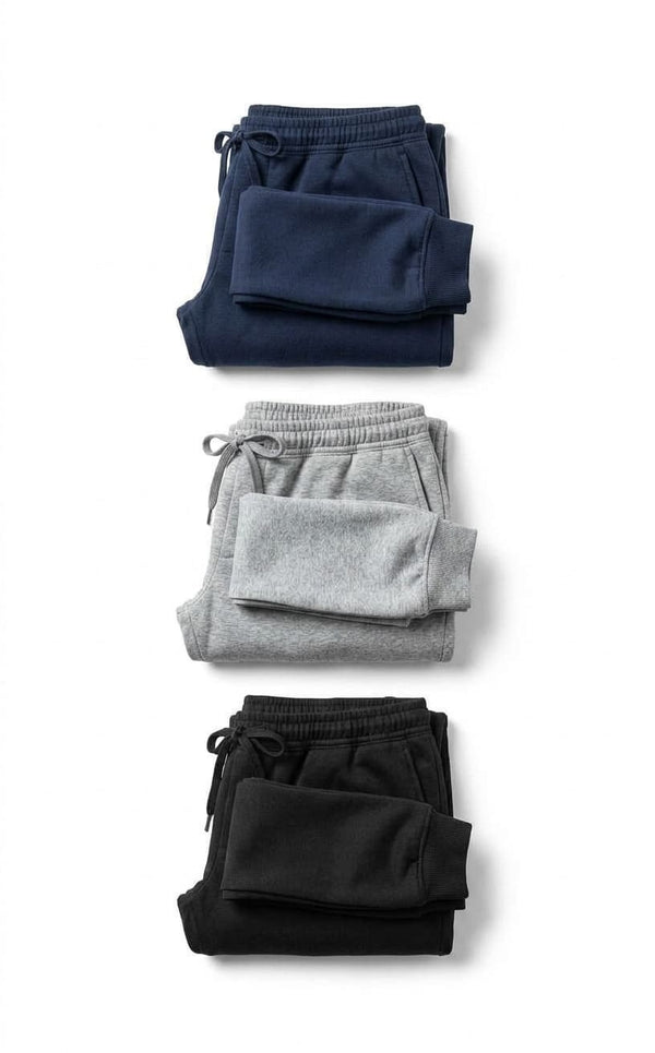 Calça de moletom masculina peluciada nas três cores disponíveis, azul marinho, cinza mescla e preto, dobradas lado a lado sobre fundo branco, mostrando o cordão do cós em cada uma